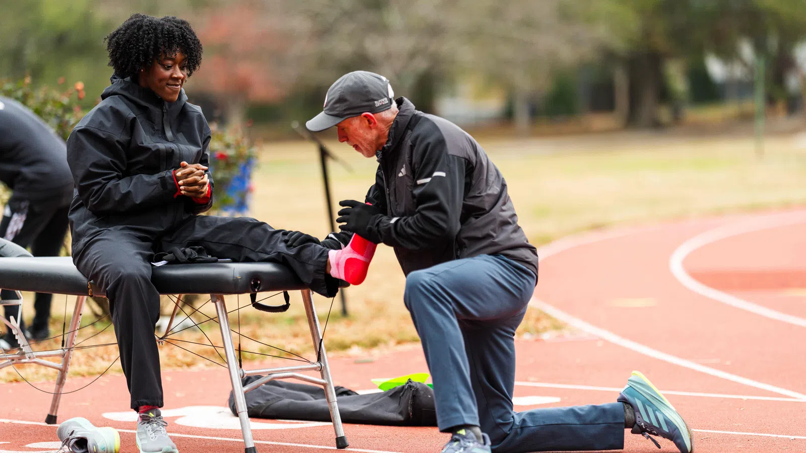 Athlete receives foot taping treatment from trainer on outdoor running track during sports rehabilitation session.