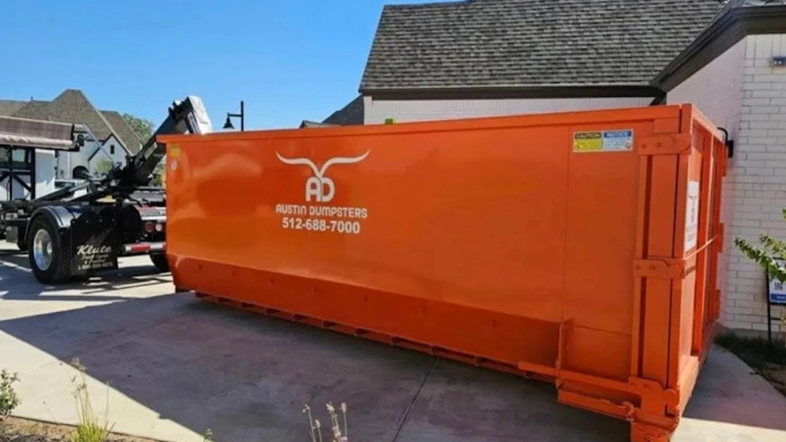 Large orange Austin Dumpsters container parked beside a residential driveway under clear blue sky