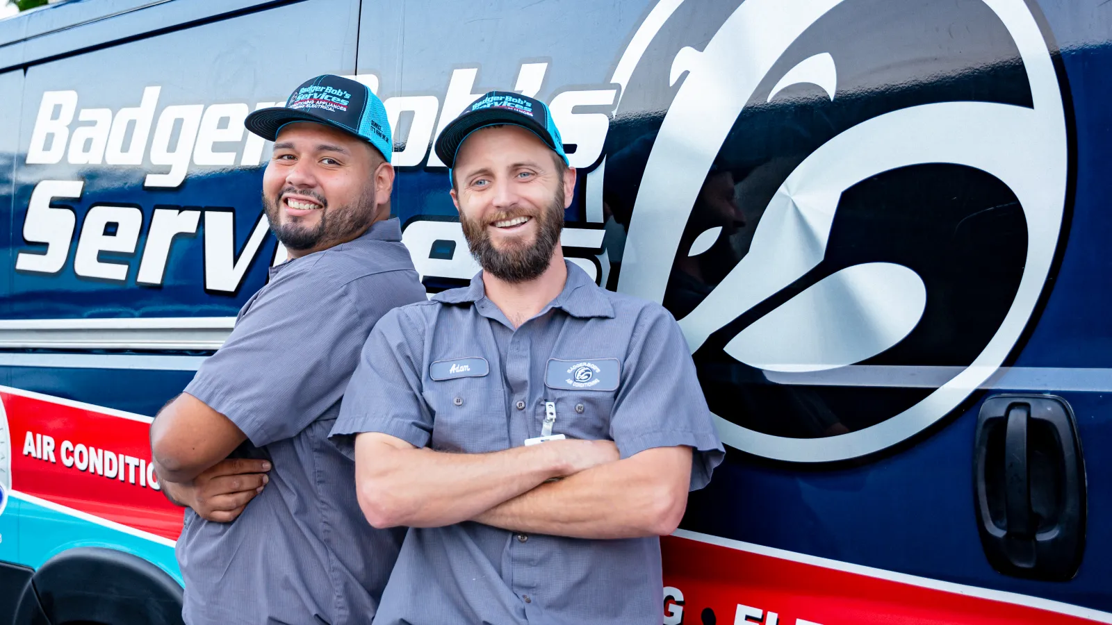 Two men discussing an air conditioning unit in a well-maintained yard, with a woman relaxing nearby.