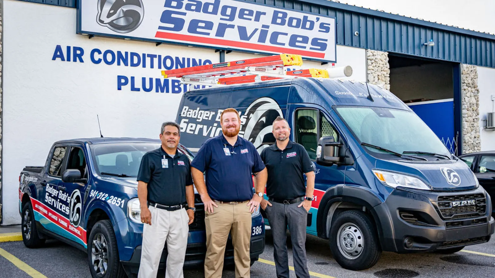 Three technicians stand in front of Badger Bob's Services pickup truck and van outside the company building.