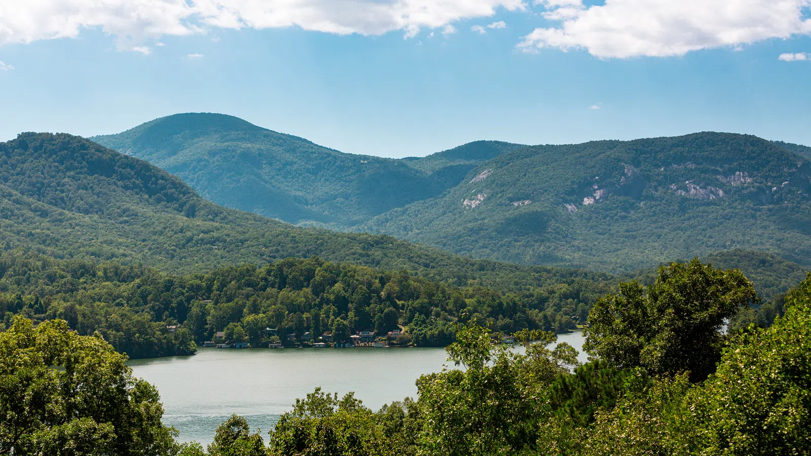 Scenic view of Lake Lure, NC  surrounded by lush green forest and mountains under a partly cloudy sky