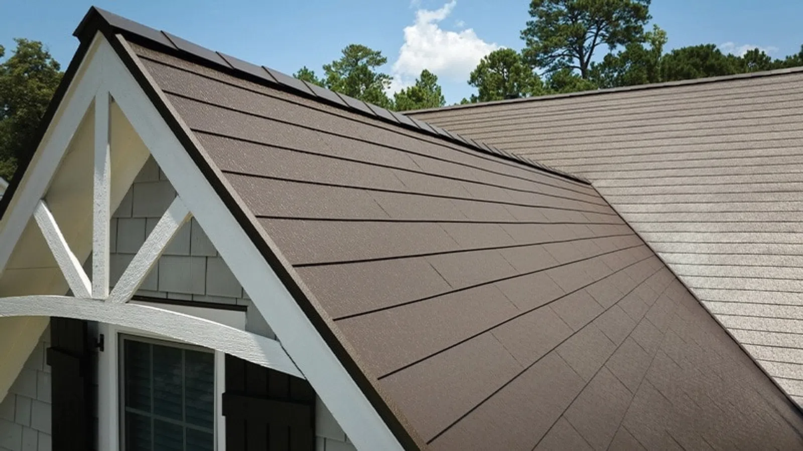 Close-up of a modern house roof with dark brown shingles and white trim under a clear blue sky.