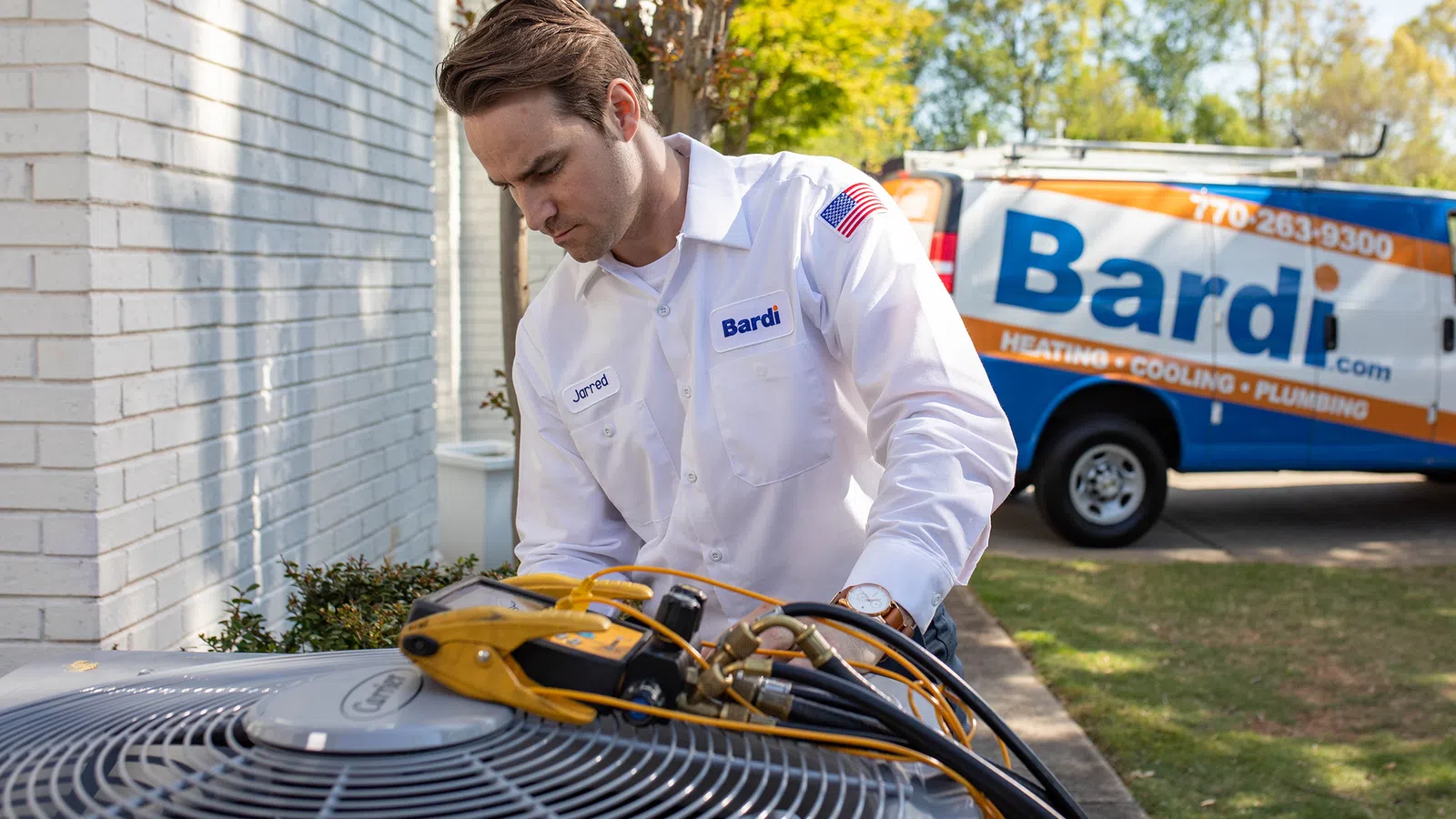 HVAC technician servicing an air conditioning unit with a service van in the background.