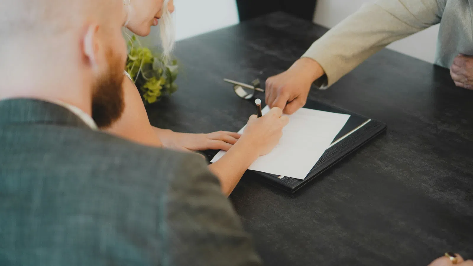 People sitting at a table with one person signing a document while another points at it.