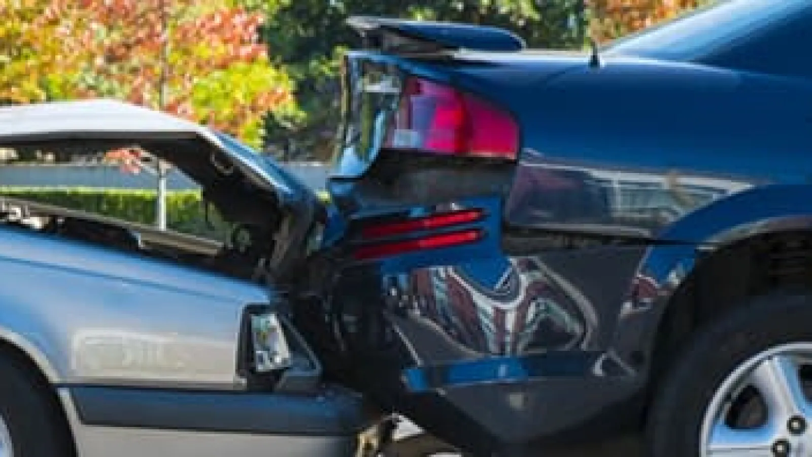 Black car rear-end collision with silver car front damage parked outside on a sunny day.