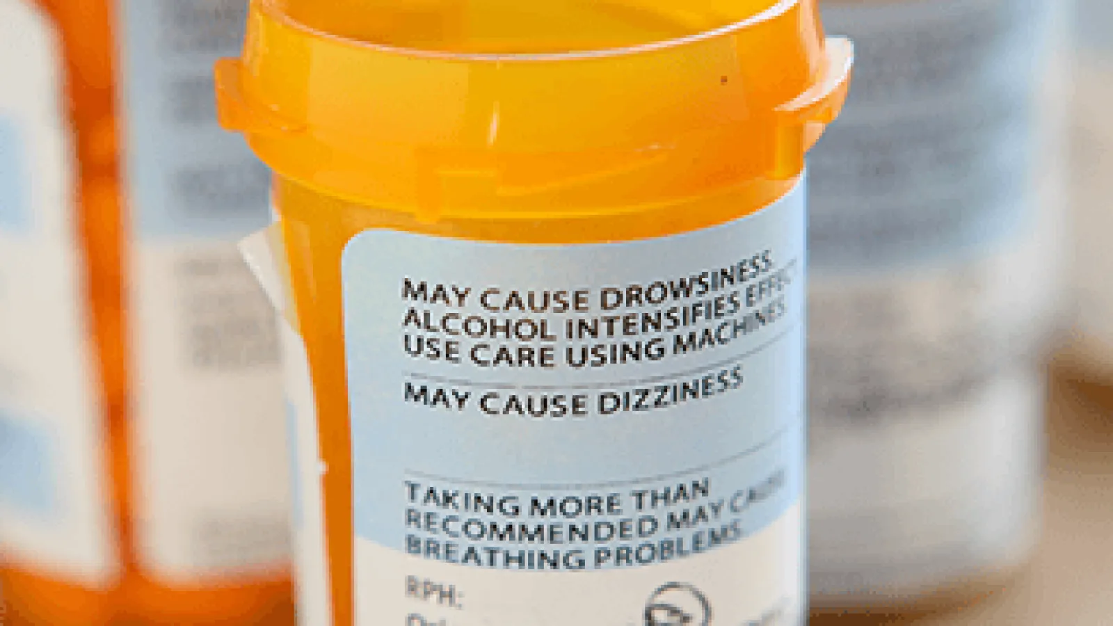 Close-up of an orange prescription bottle with warning labels about drowsiness, dizziness, and alcohol effects.
