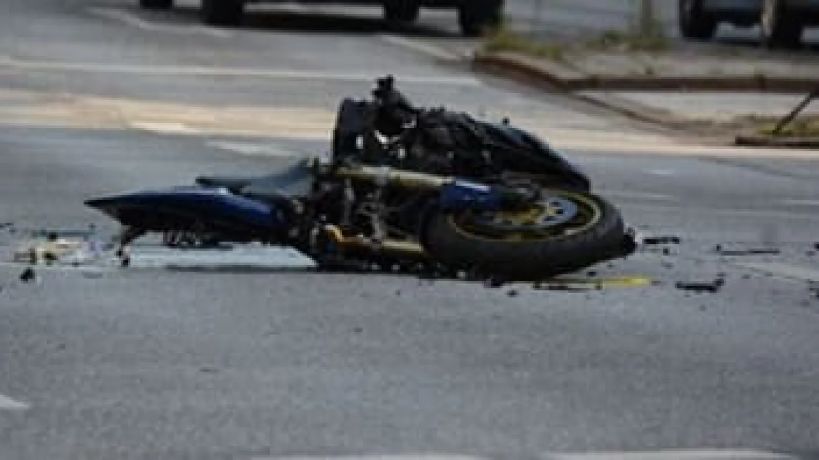 Damaged motorcycle lying on its side on a city street after an accident with debris scattered around.