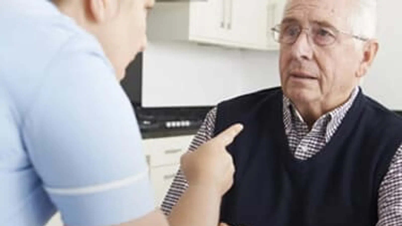 Caregiver talking seriously to elderly man in a home kitchen setting showing concern and support.