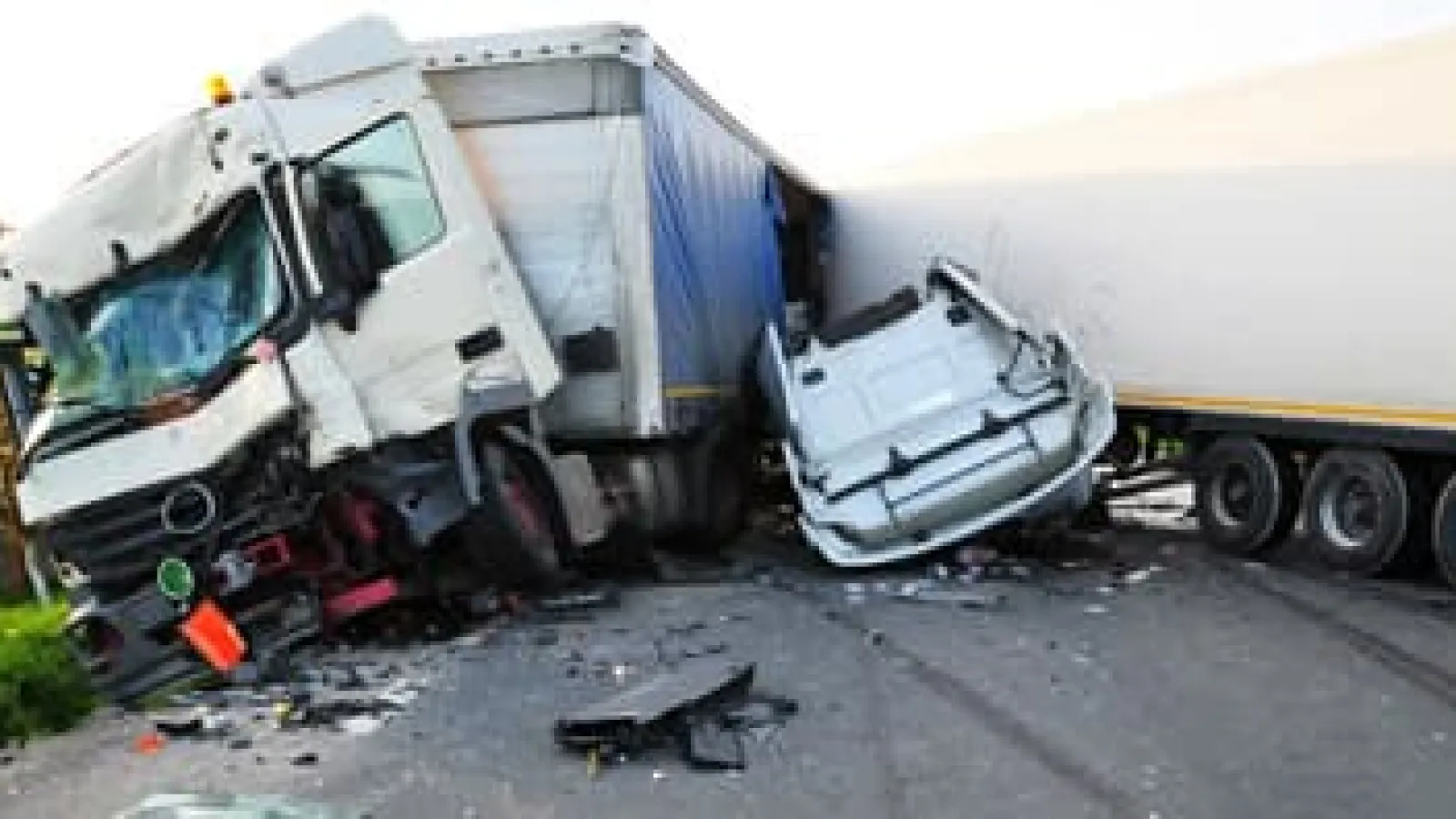Two semi-trucks involved in a major roadside collision with significant damage and debris on the asphalt road.