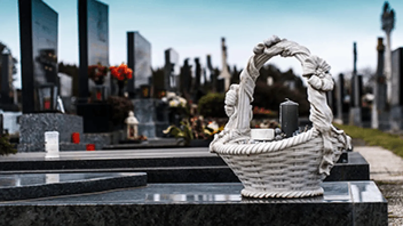 White decorative basket with flowers and candle on a black granite grave in a cemetery.