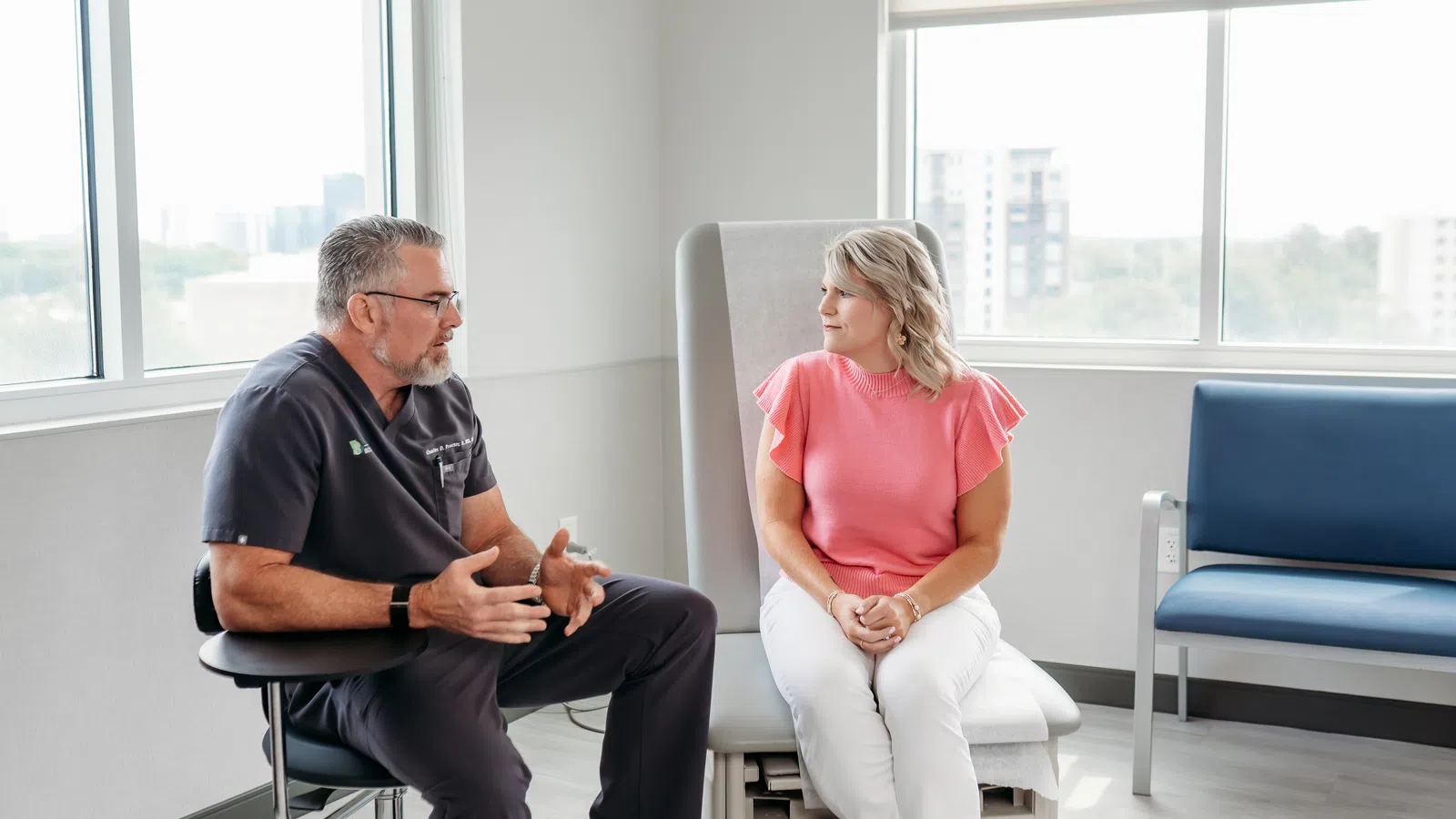Doctor discussing medical advice with a female patient in a bright, modern clinic room with large windows.