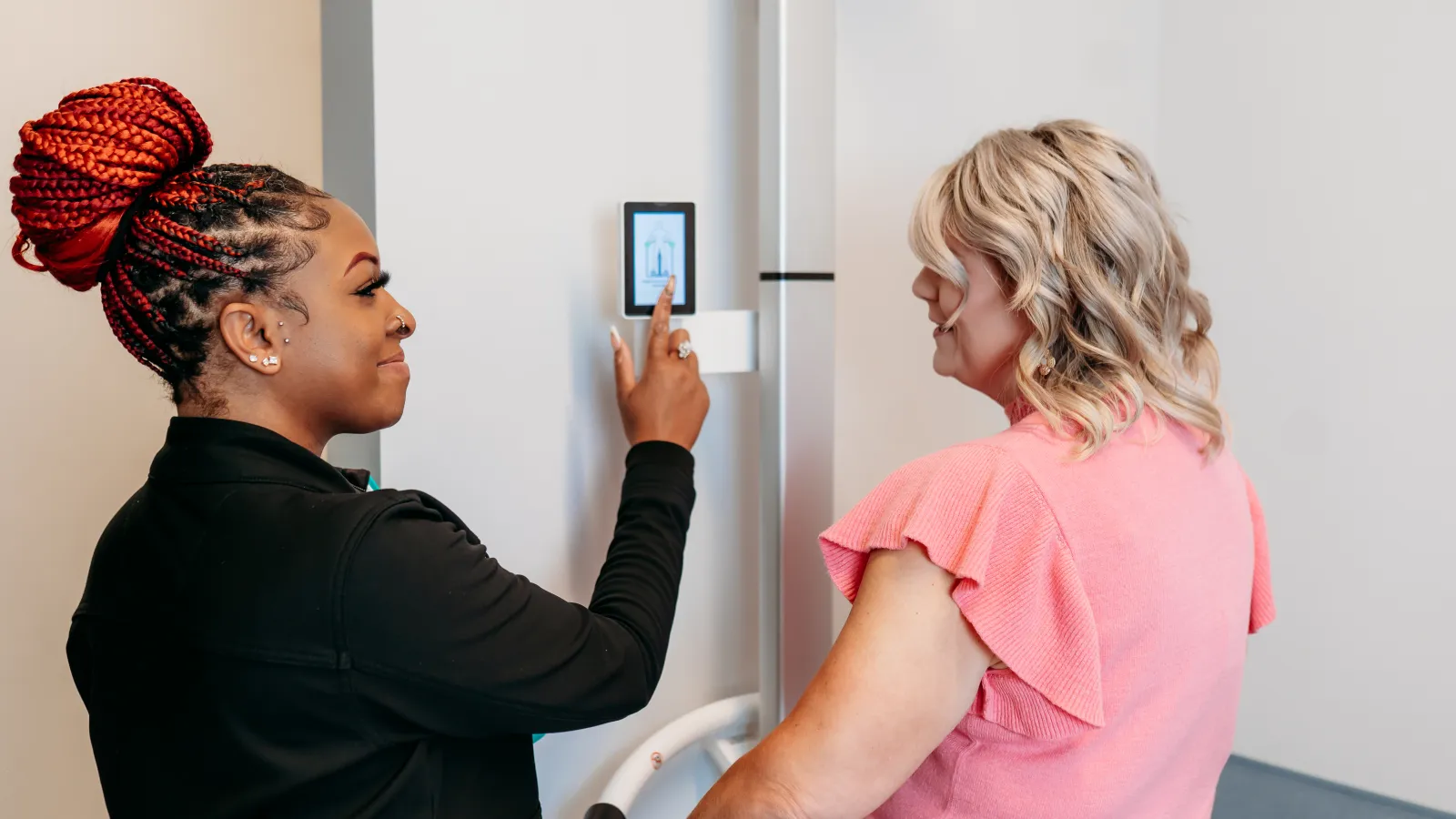 Two women interacting with a digital touchscreen panel on a modern refrigerator in a kitchen setting