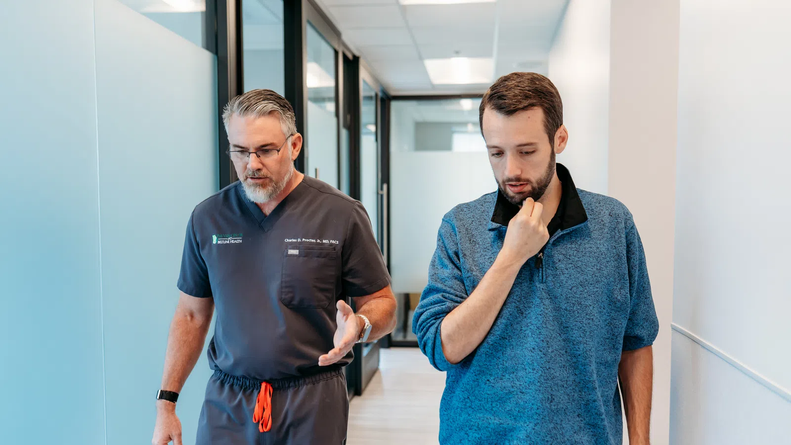 Doctor in scrubs discussing with a patient walking down a medical office hallway