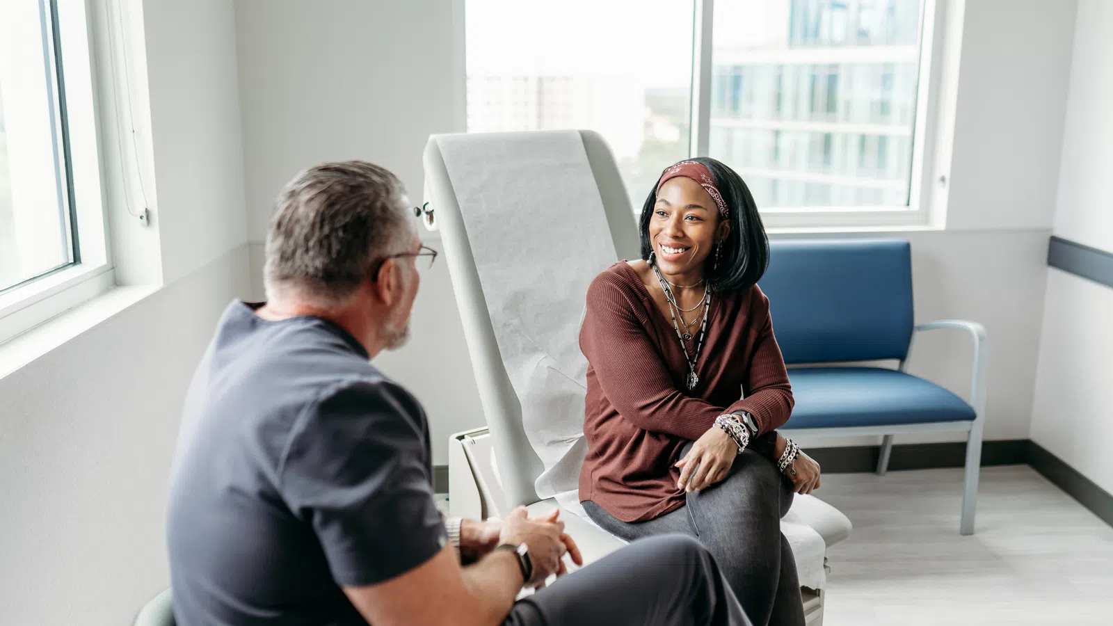 Smiling woman talking with male doctor in modern medical office with natural light and city view windows