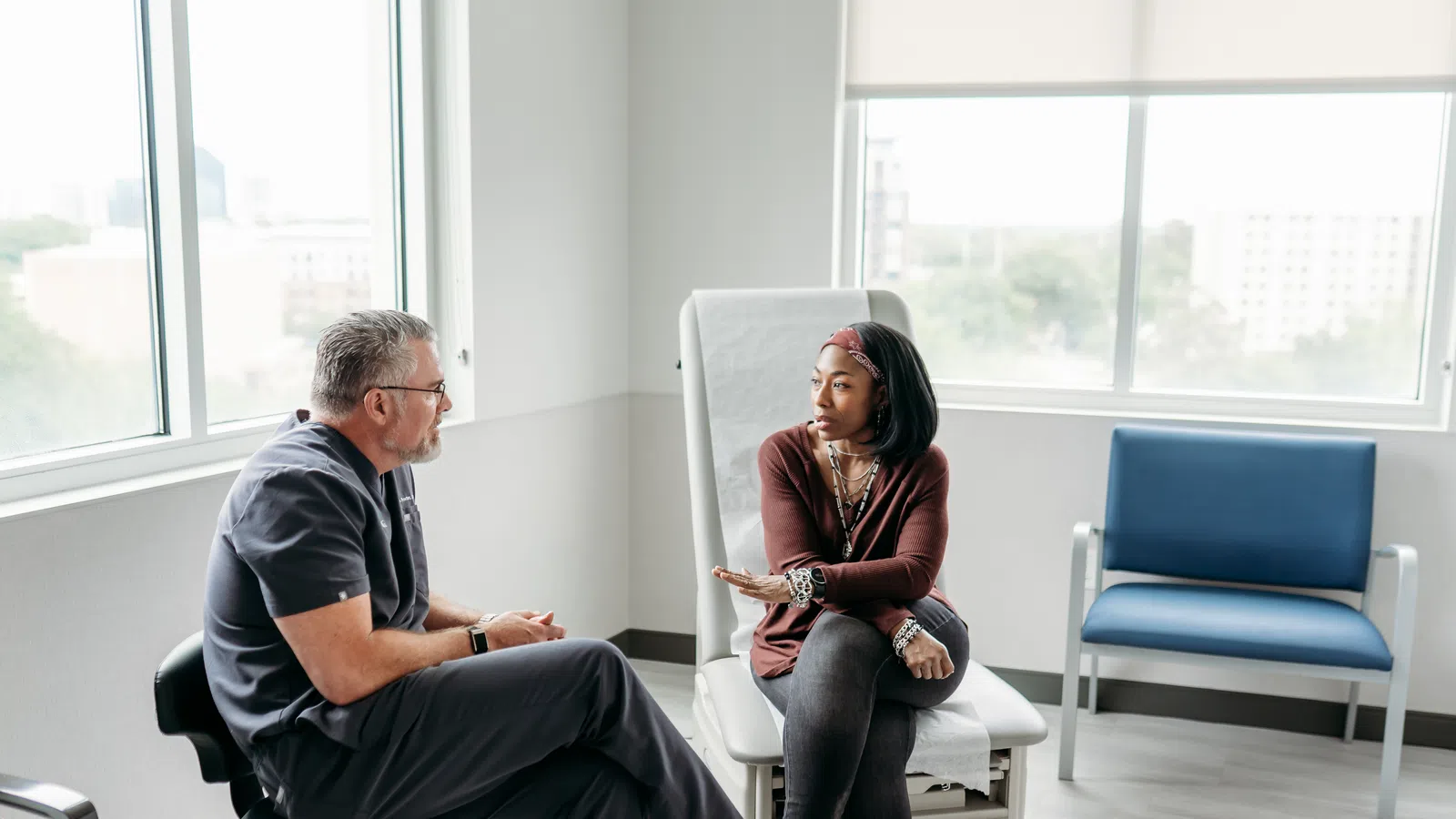 Female patient discussing health concerns with doctor in bright medical office with large windows.