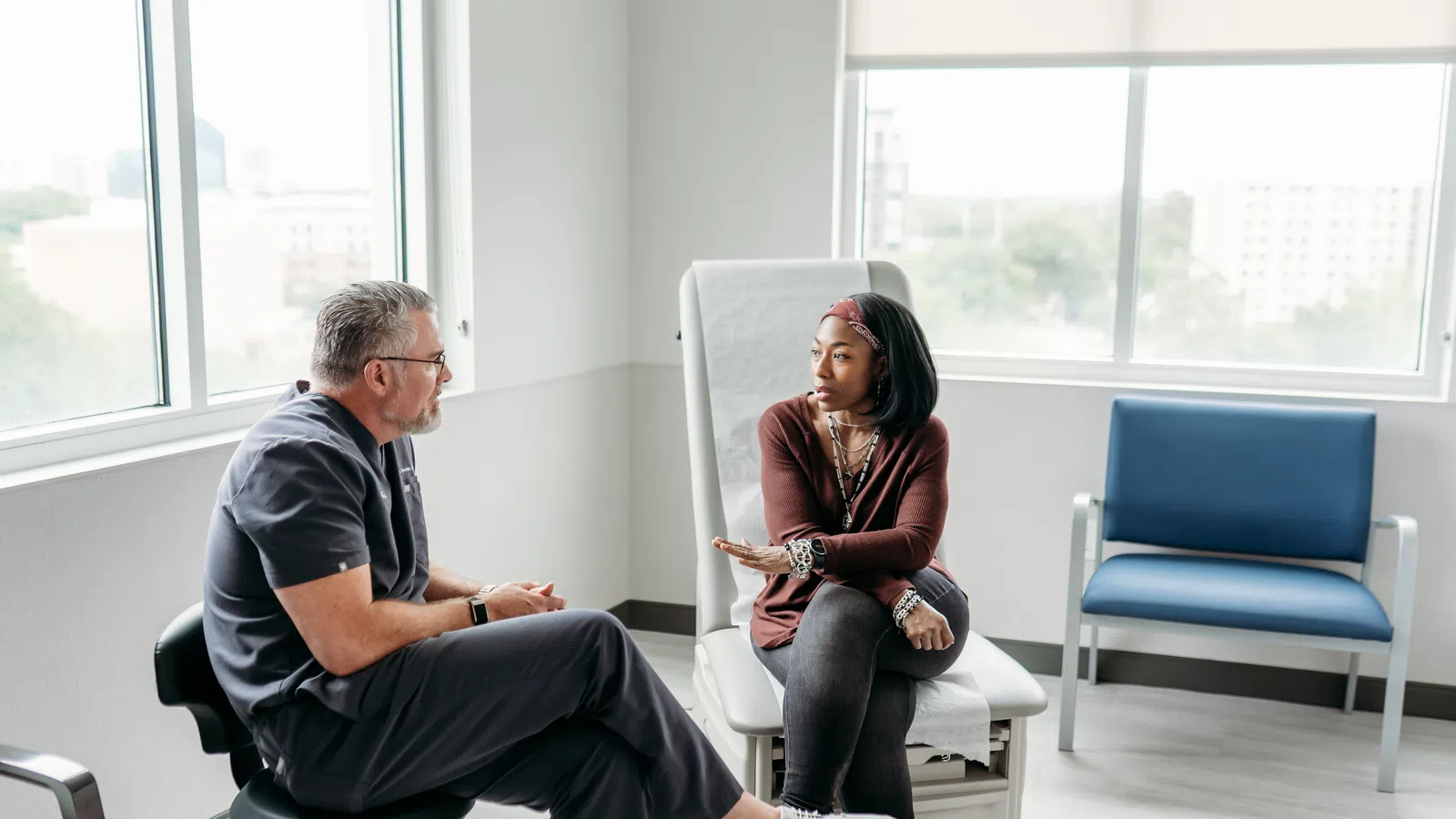 Female patient discussing health concerns with doctor in bright medical office with large windows.