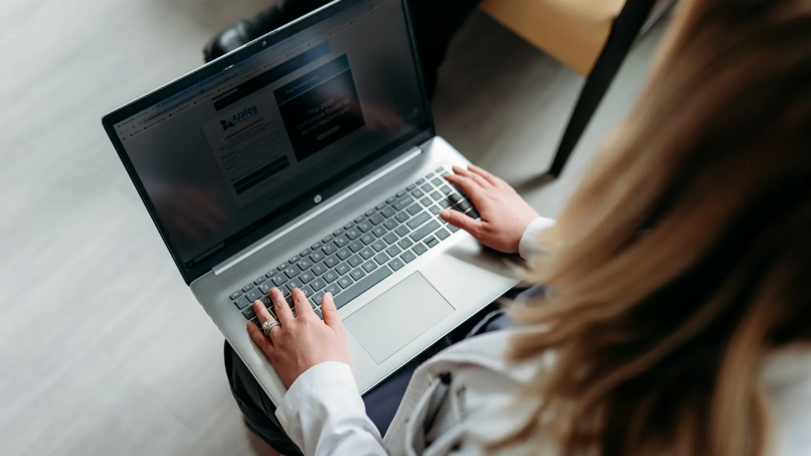 Person using a laptop with both hands typing on the keyboard in a bright indoor space.