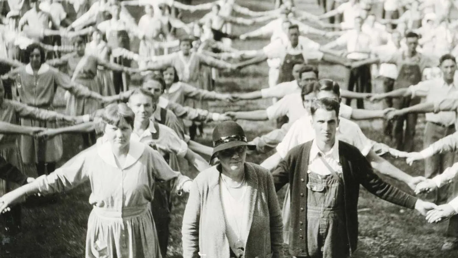 Large group of men and women standing in rows outdoors holding hands with arms extended