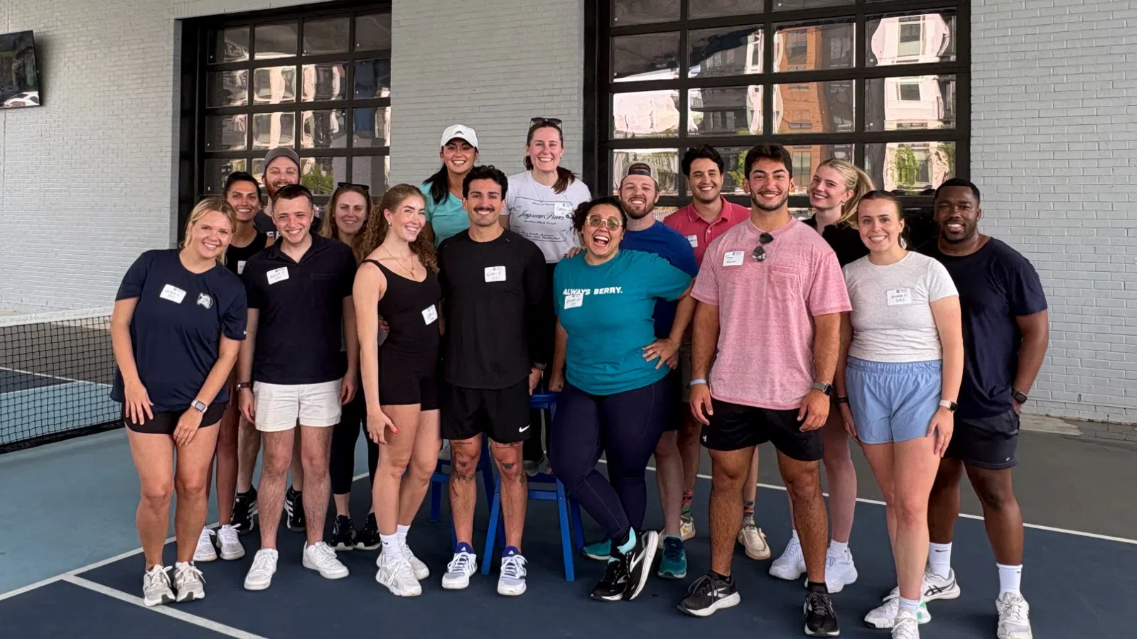 Group of adults posing on an indoor pickleball court under Pickle and Social sign in sportswear.