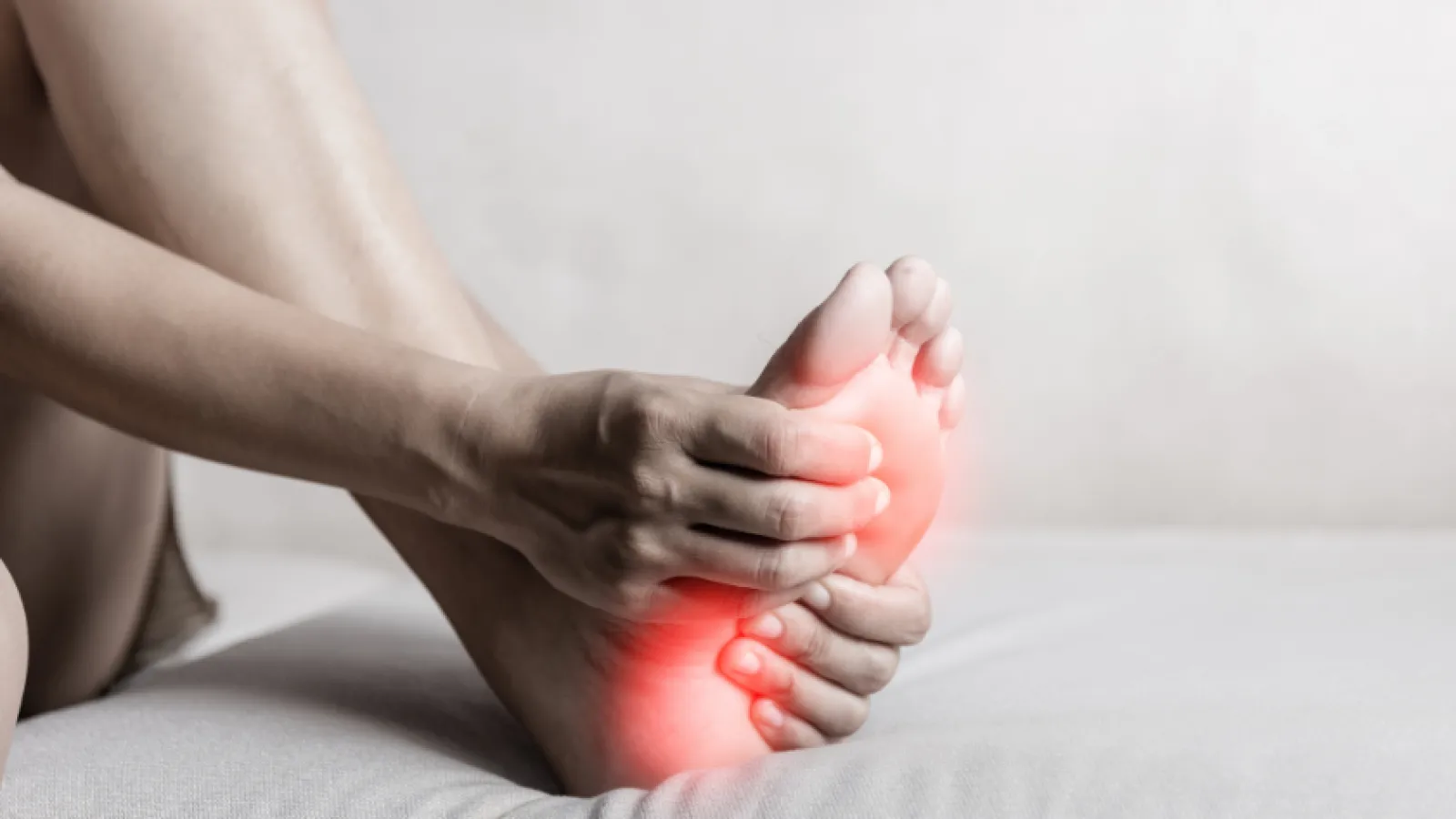 Person holding foot with red glow highlighting pain area, indicating foot discomfort or injury.