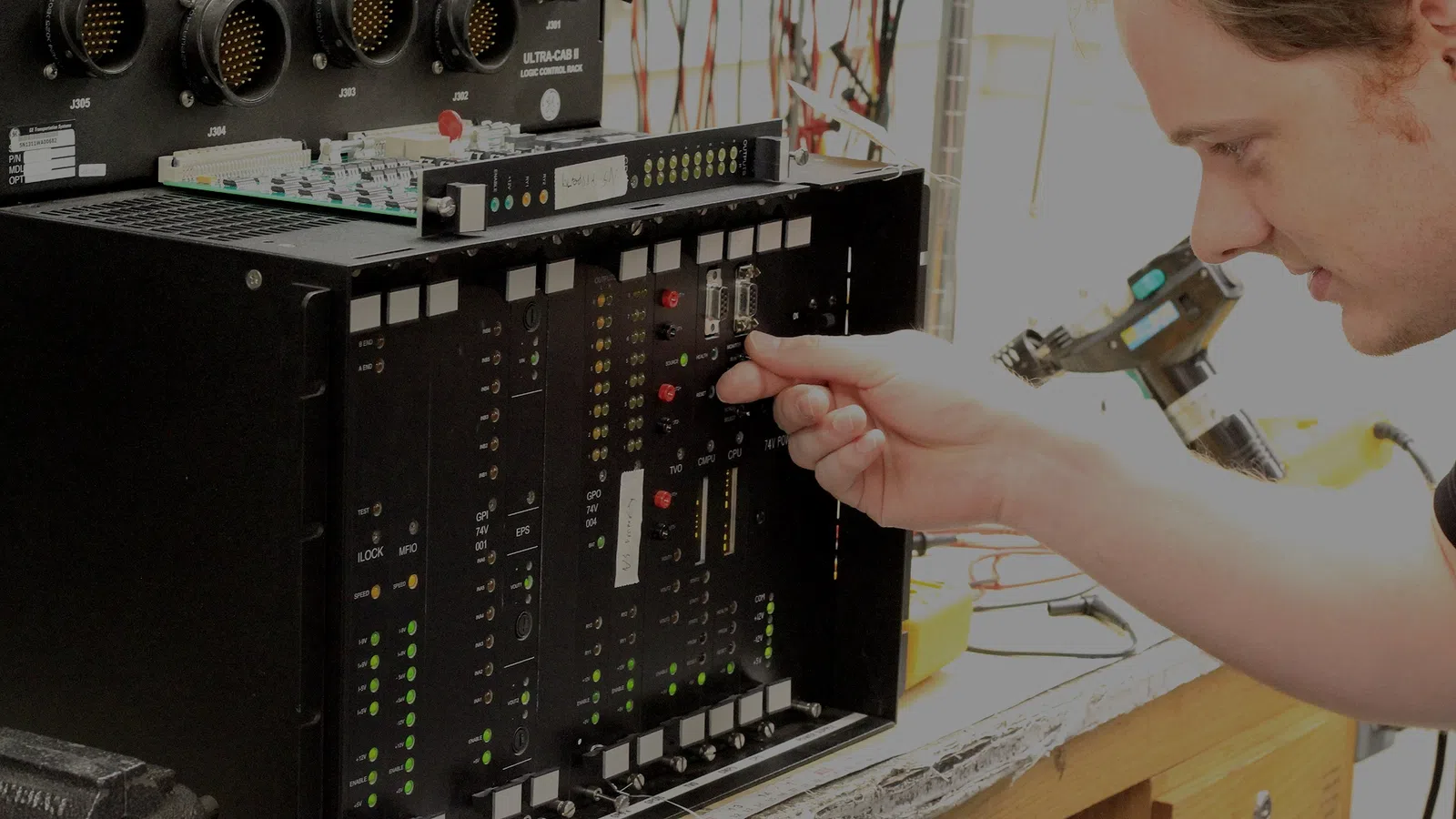 Technician adjusting switches on a complex electronic control panel in a workshop setting.