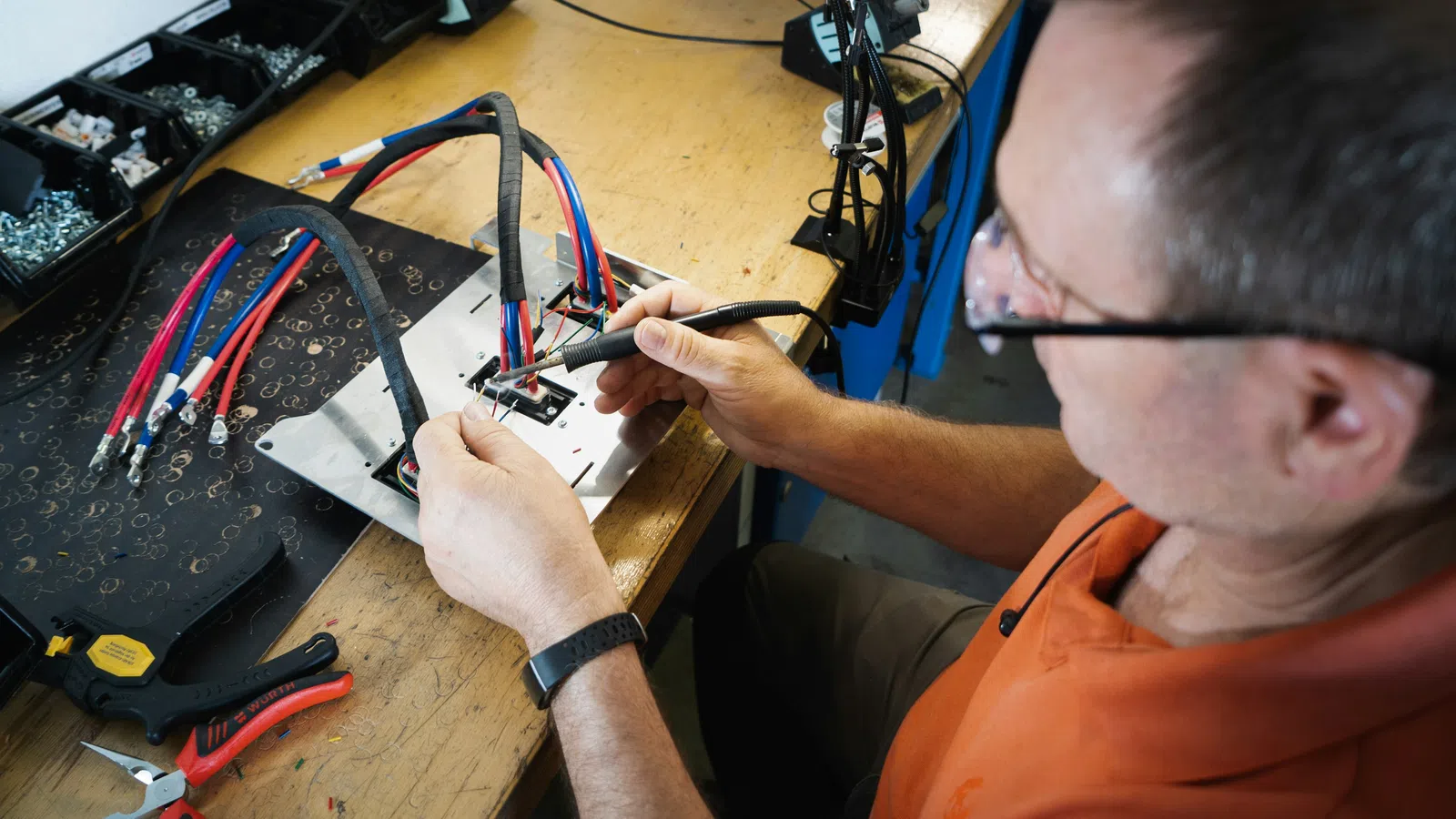Man using soldering iron to work on electronic wiring at a cluttered workbench