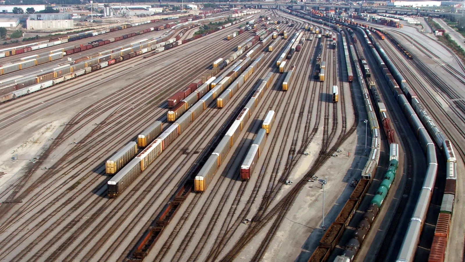 Aerial view of a large rail yard with multiple train tracks and freight trains parked on them under a clear sky.