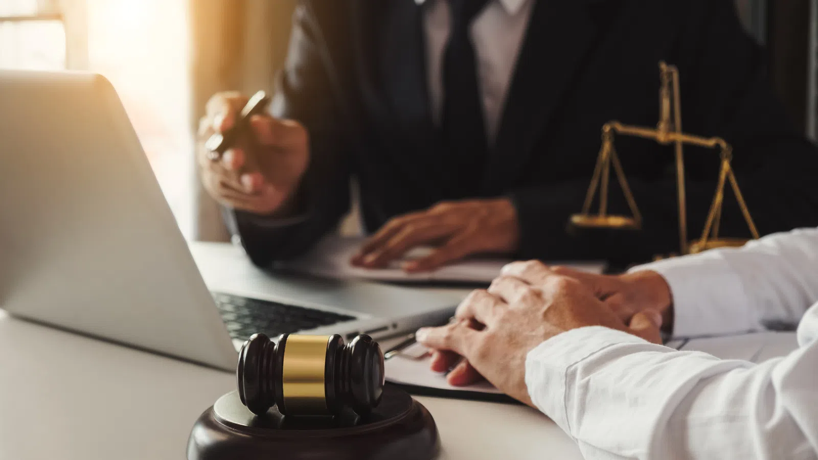 Lawyer and client consulting in office with gavel and scales of justice on desk near laptop