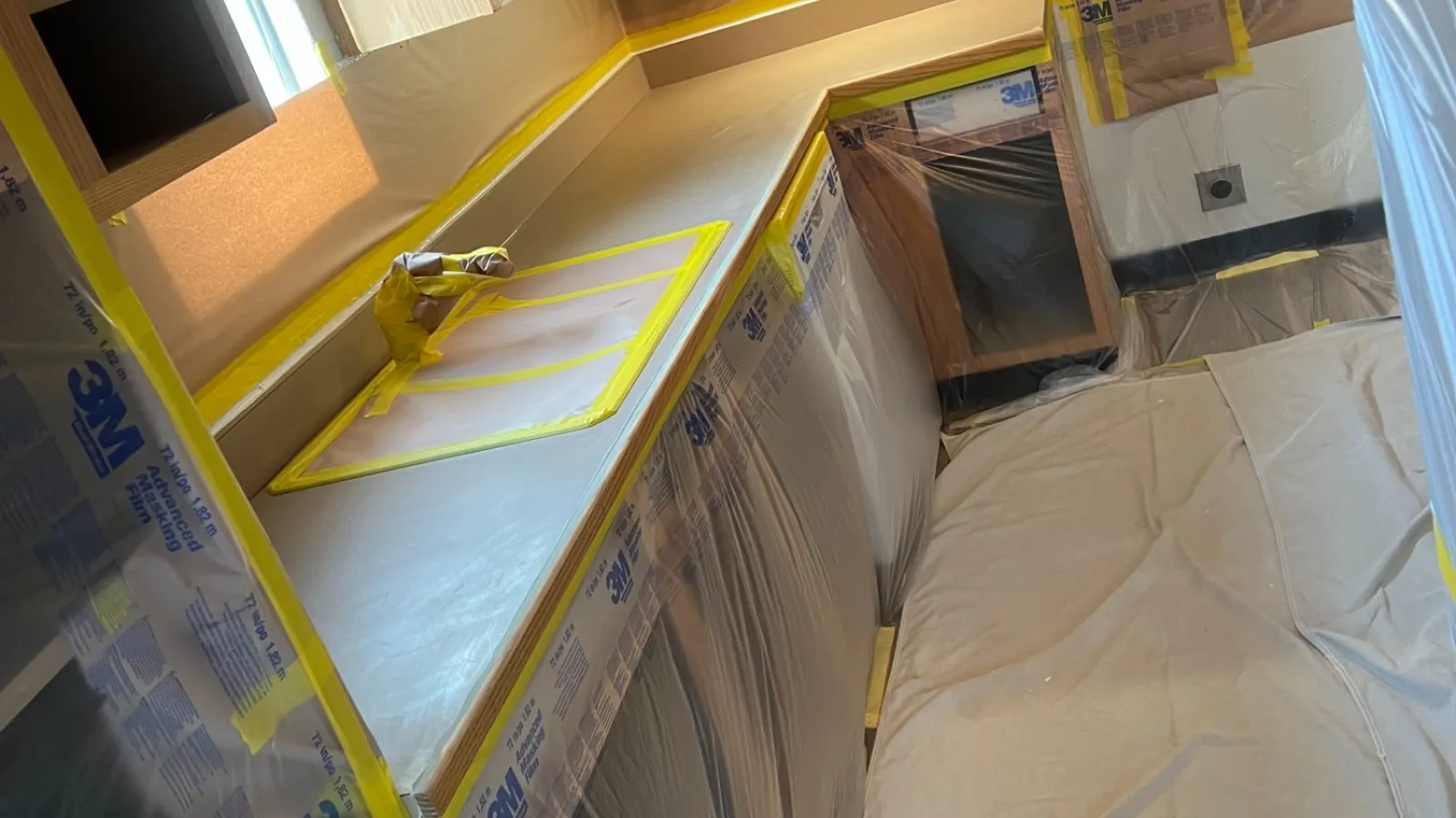 Kitchen cabinets and appliances covered with plastic and tape for protection during renovation or painting work.