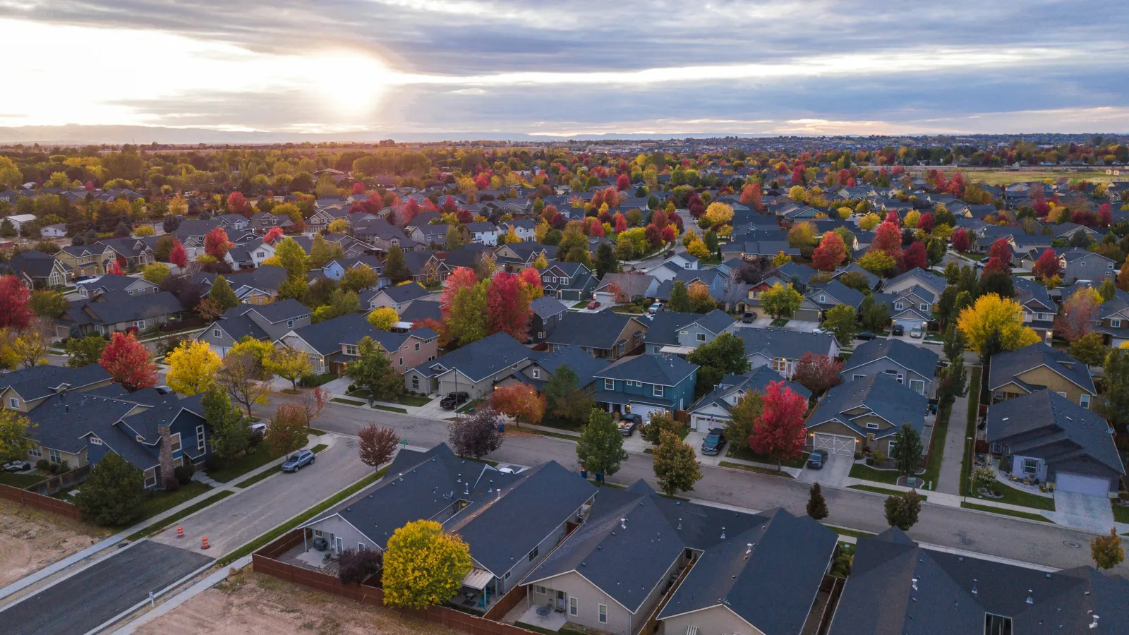 Aerial view of suburban neighborhood with many houses and colorful autumn trees under a cloudy sunset sky.