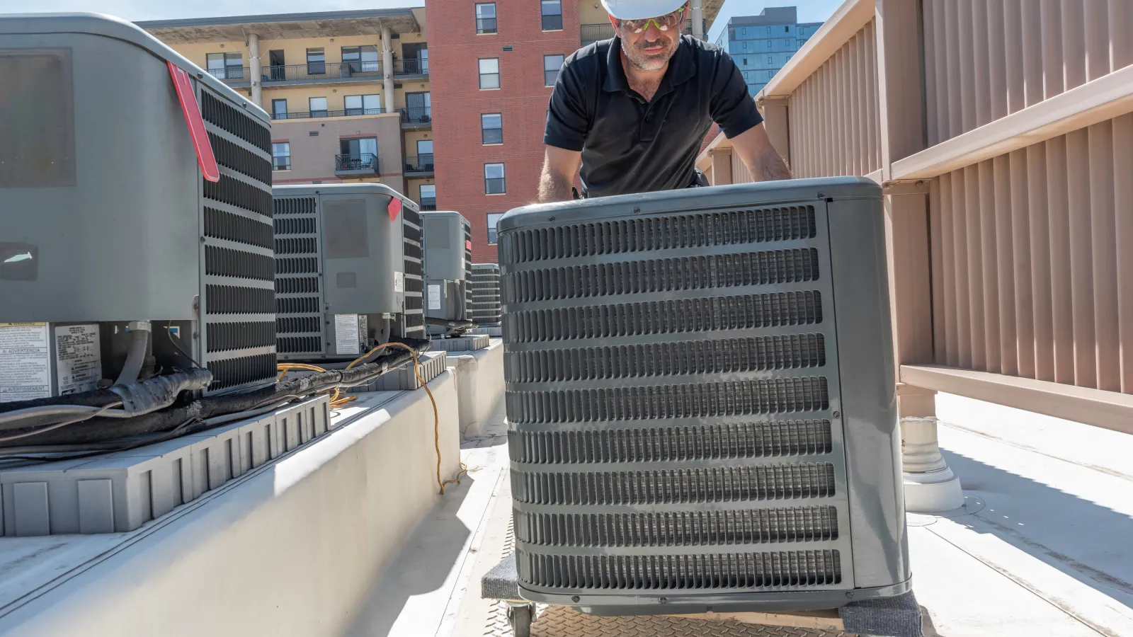 Technician installing or servicing HVAC unit on a rooftop in an urban setting.