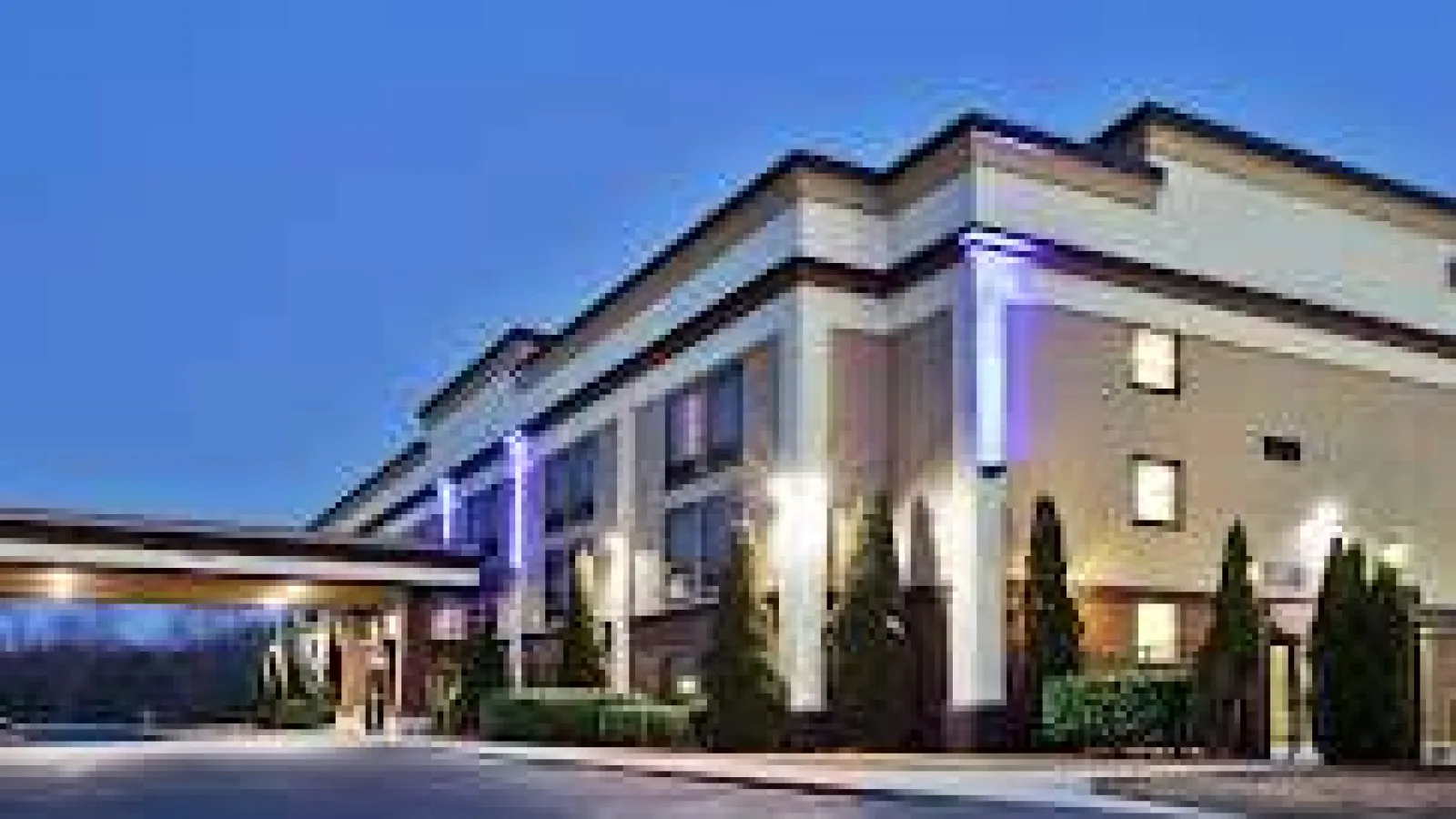 Exterior view of a modern hotel building at dusk with illuminated entrance and landscaping
