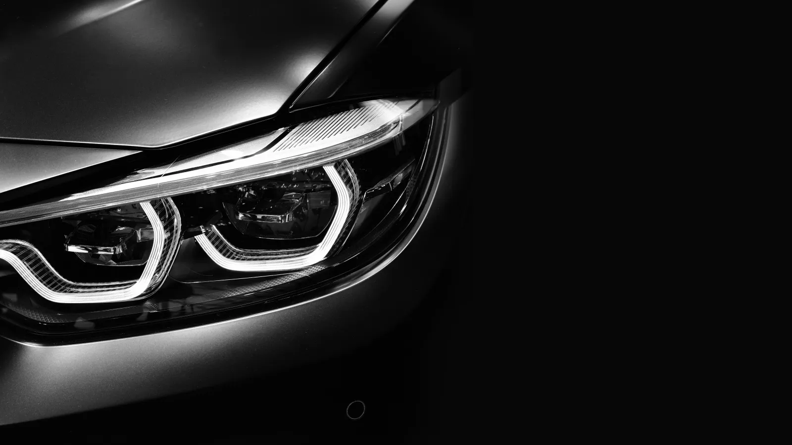 Close-up of a sleek car's illuminated LED headlights with sharp design accents on a dark background