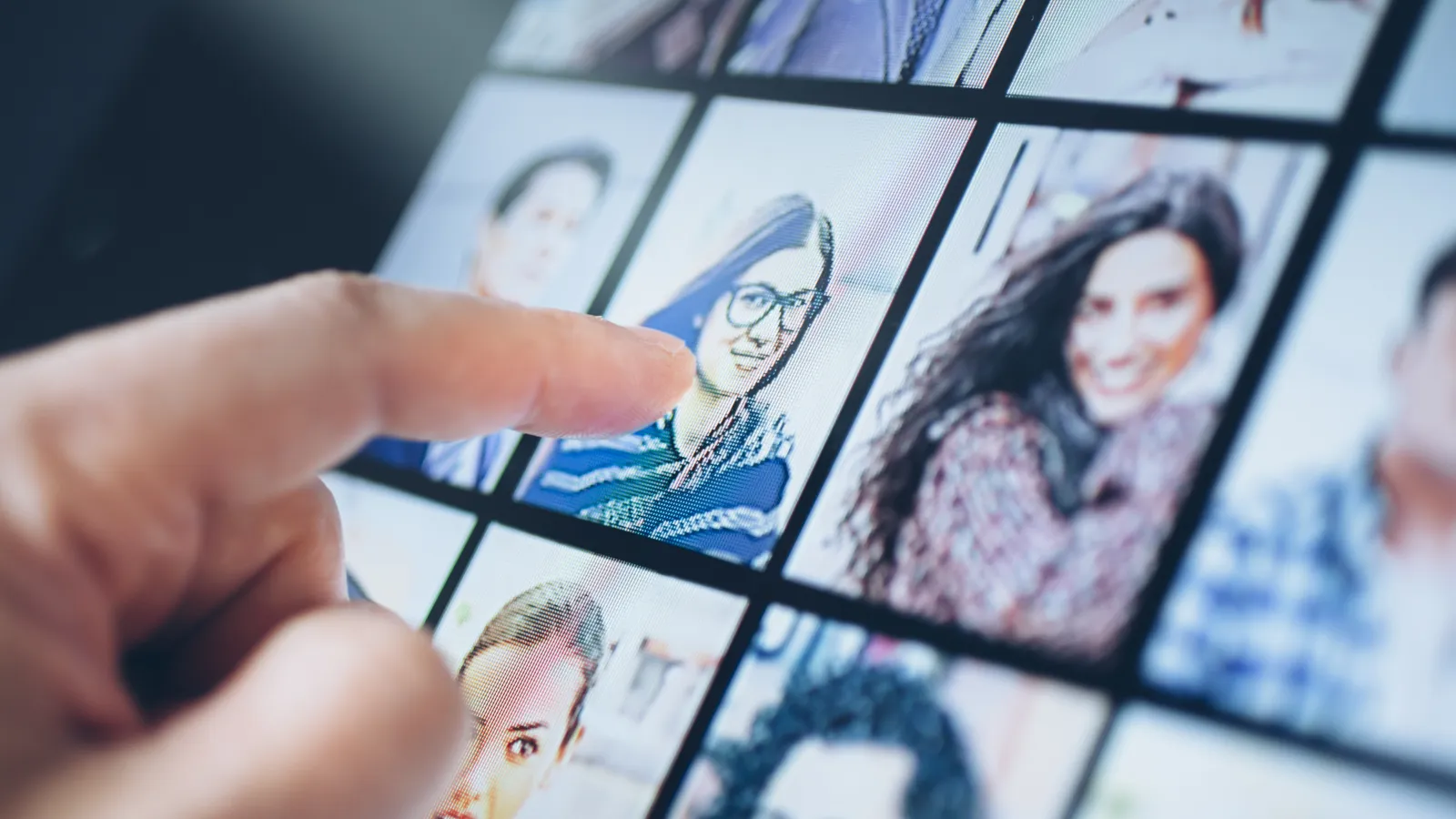 Finger selecting a woman's profile picture on a digital screen with multiple headshots in a grid layout.