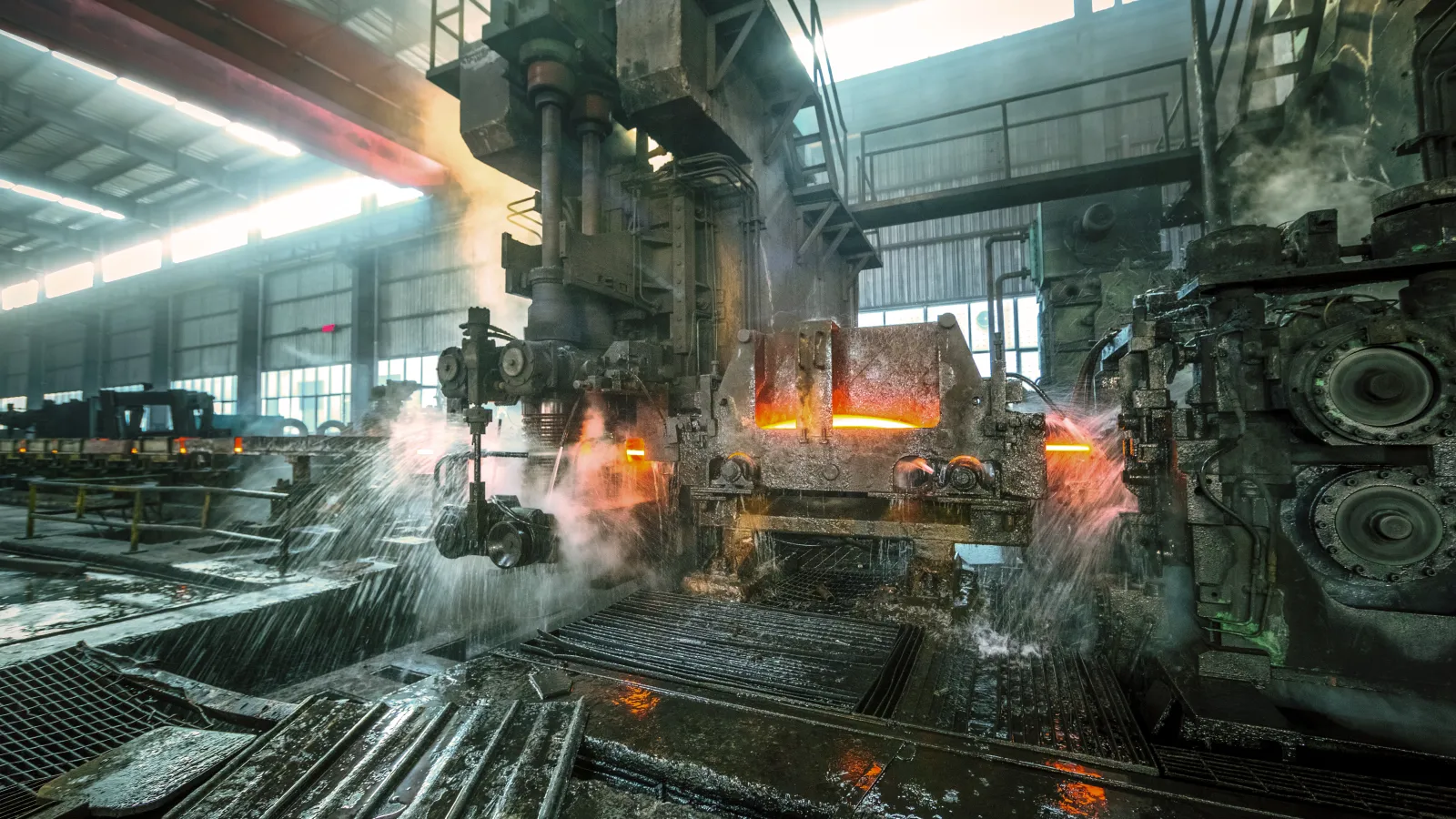 Industrial steel manufacturing plant with machinery and steam creating an intense atmosphere.