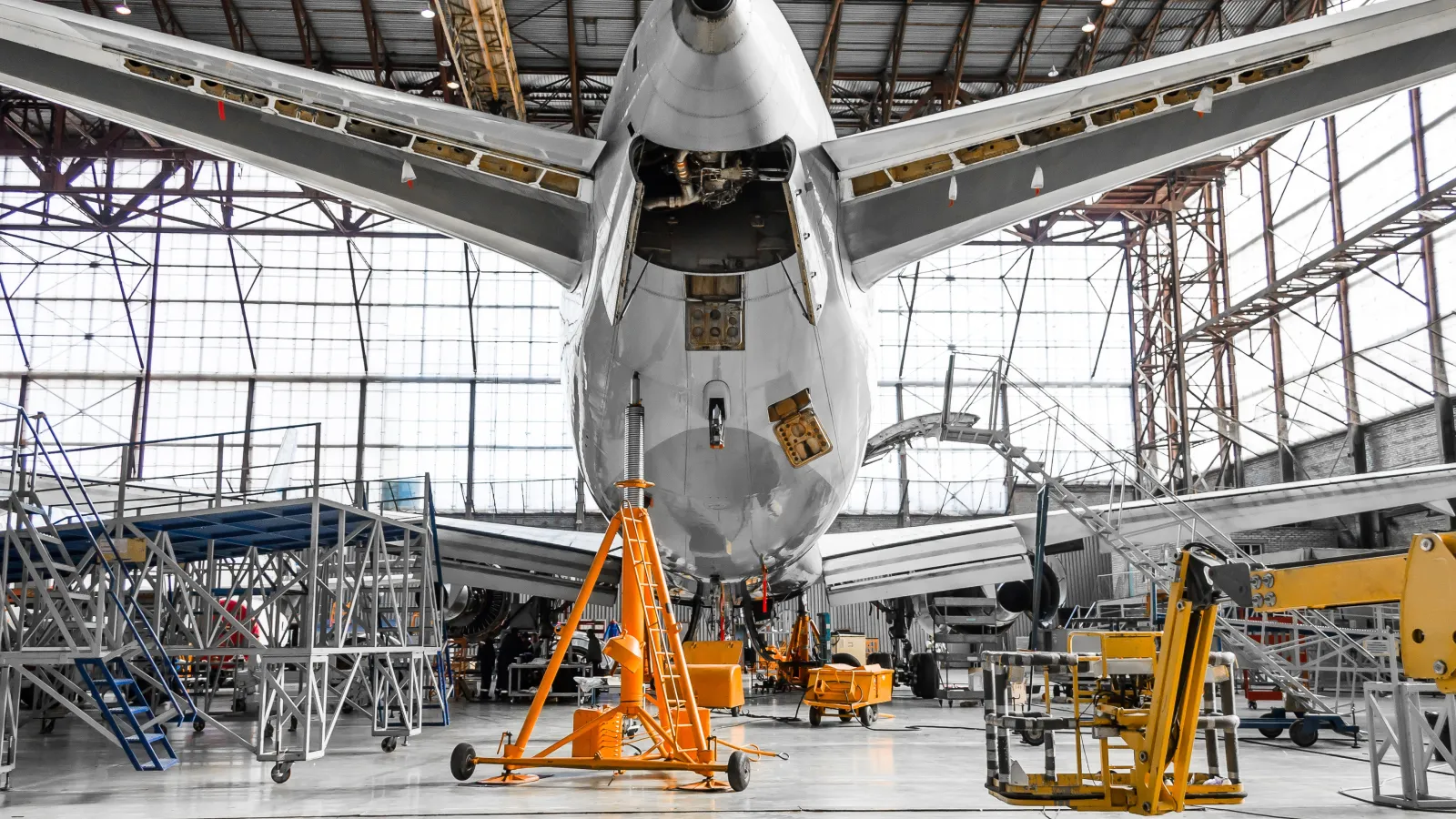 Rear view of an airplane undergoing maintenance inside a large hangar with equipment and scaffolding