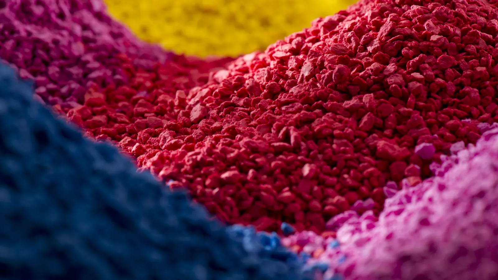 Close-up of colorful pigment powder piles in red, blue, pink, purple, and yellow hues under soft lighting