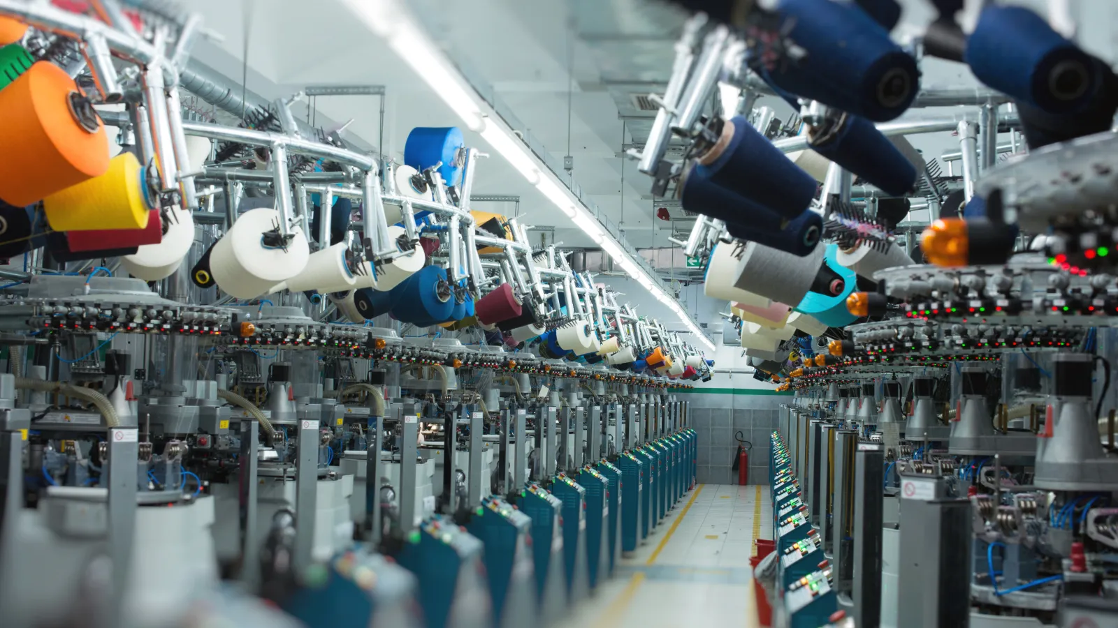 Interior view of a textile factory with rows of automated knitting machines and colorful yarn spools.