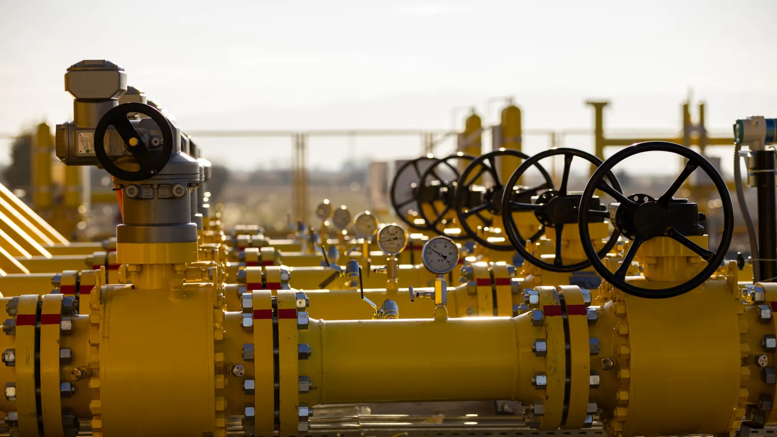 Yellow industrial gas pipelines with valves and pressure gauges in an outdoor setting under daylight.