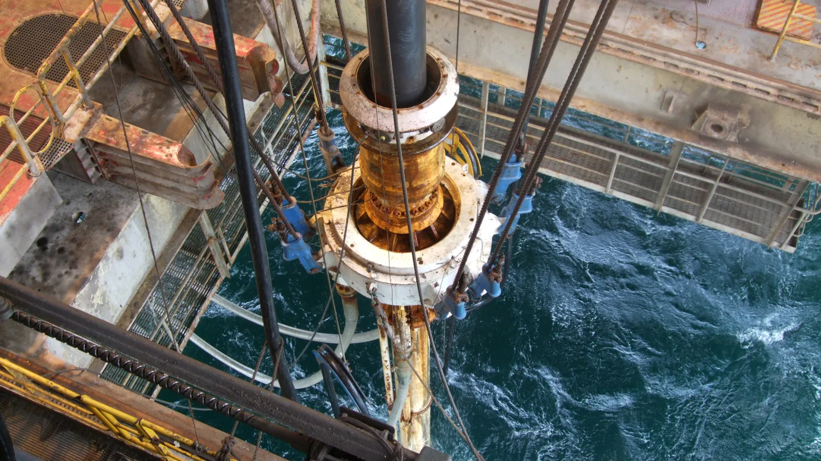 View from above an offshore drilling platform showing equipment and turbulent ocean water below.