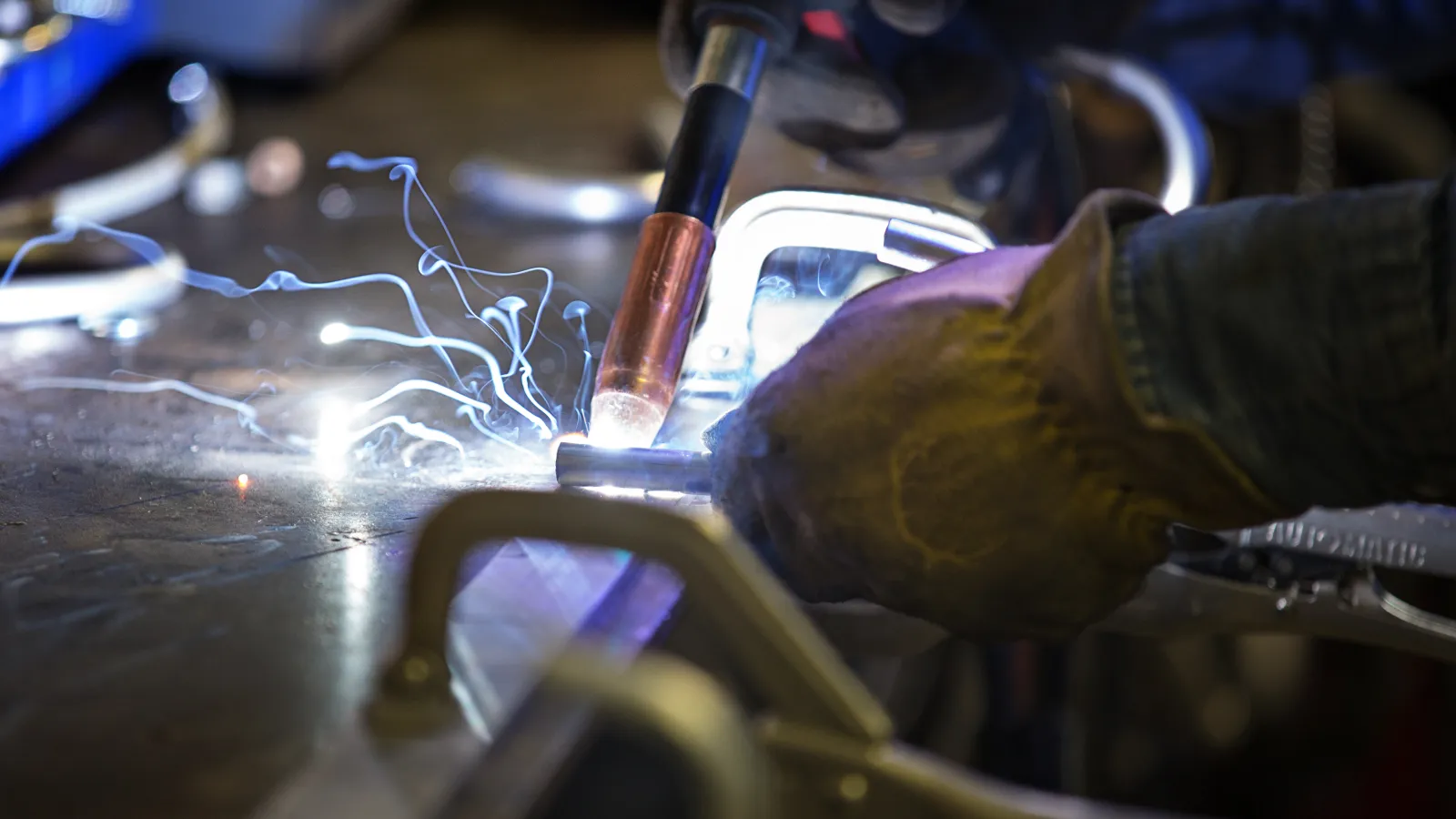 Close-up of welder wearing gloves using a welding torch creating sparks on metal surface in workshop.