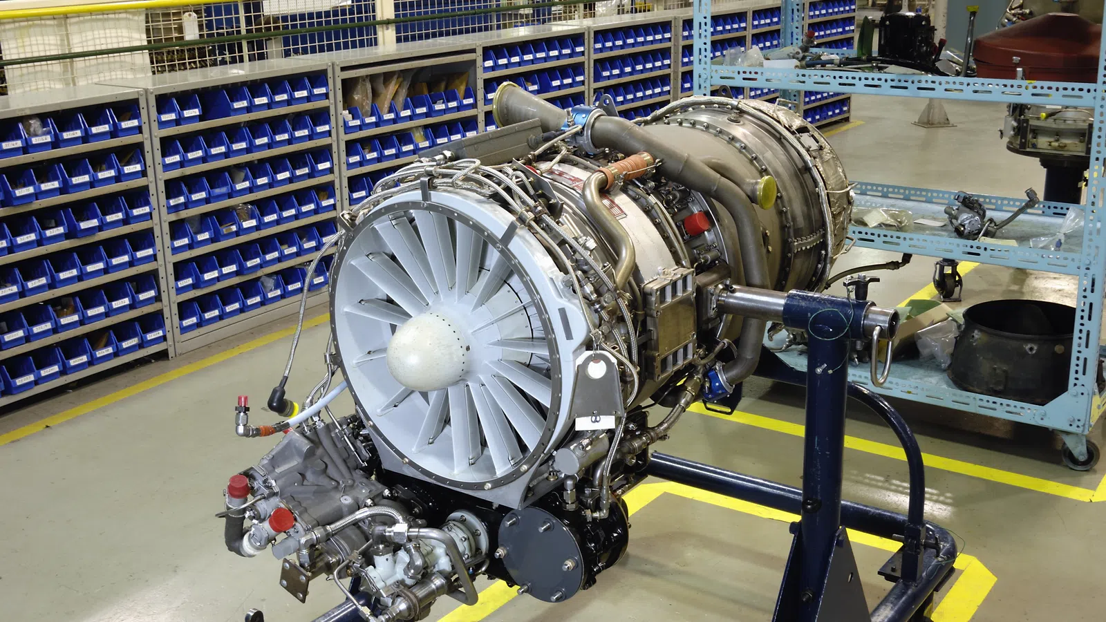 Industrial jet engine turbine displayed in a workshop with blue shelving and tools in the background
