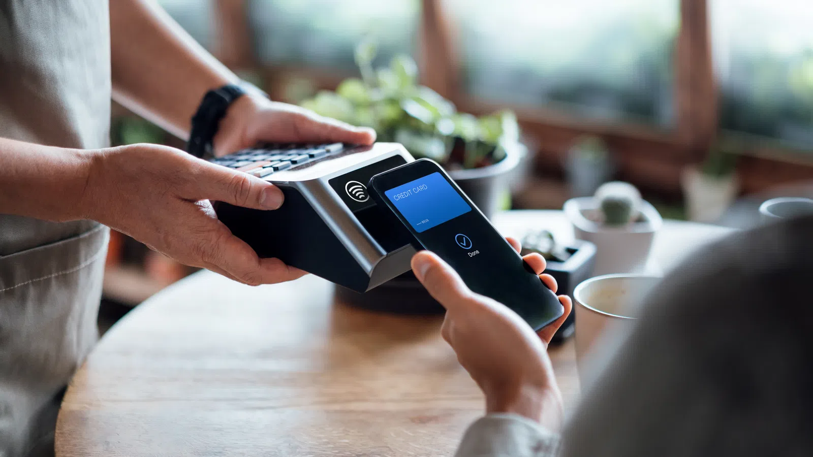 Customer making contactless payment with smartphone on payment terminal at cafe counter.