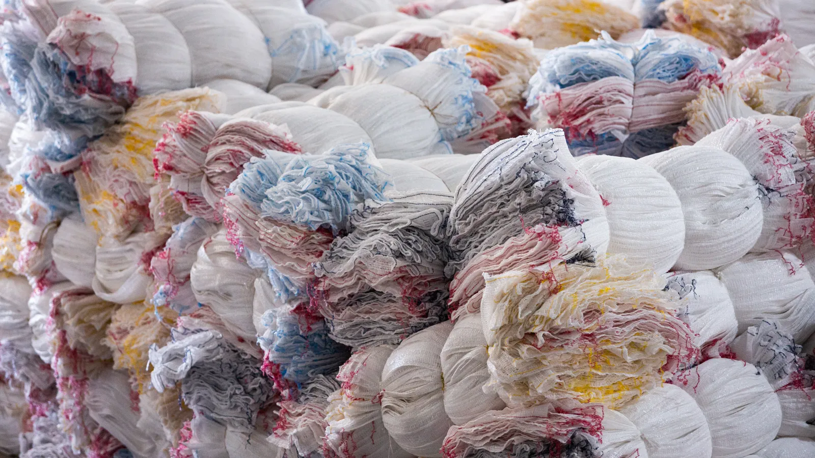 Bundles of colorful, stacked fabric or textile waste ready for recycling or processing in a factory setting.