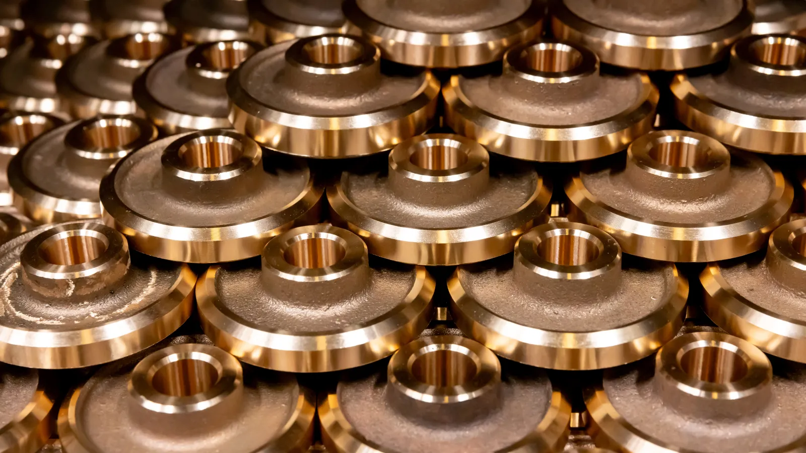 Stacked shiny bronze metal machine parts with circular shapes arranged in a pattern.