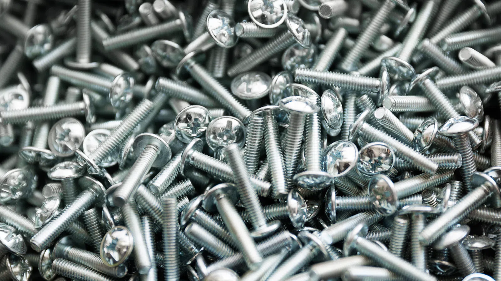 Pile of shiny silver metal screws with round Phillips heads closely packed together.