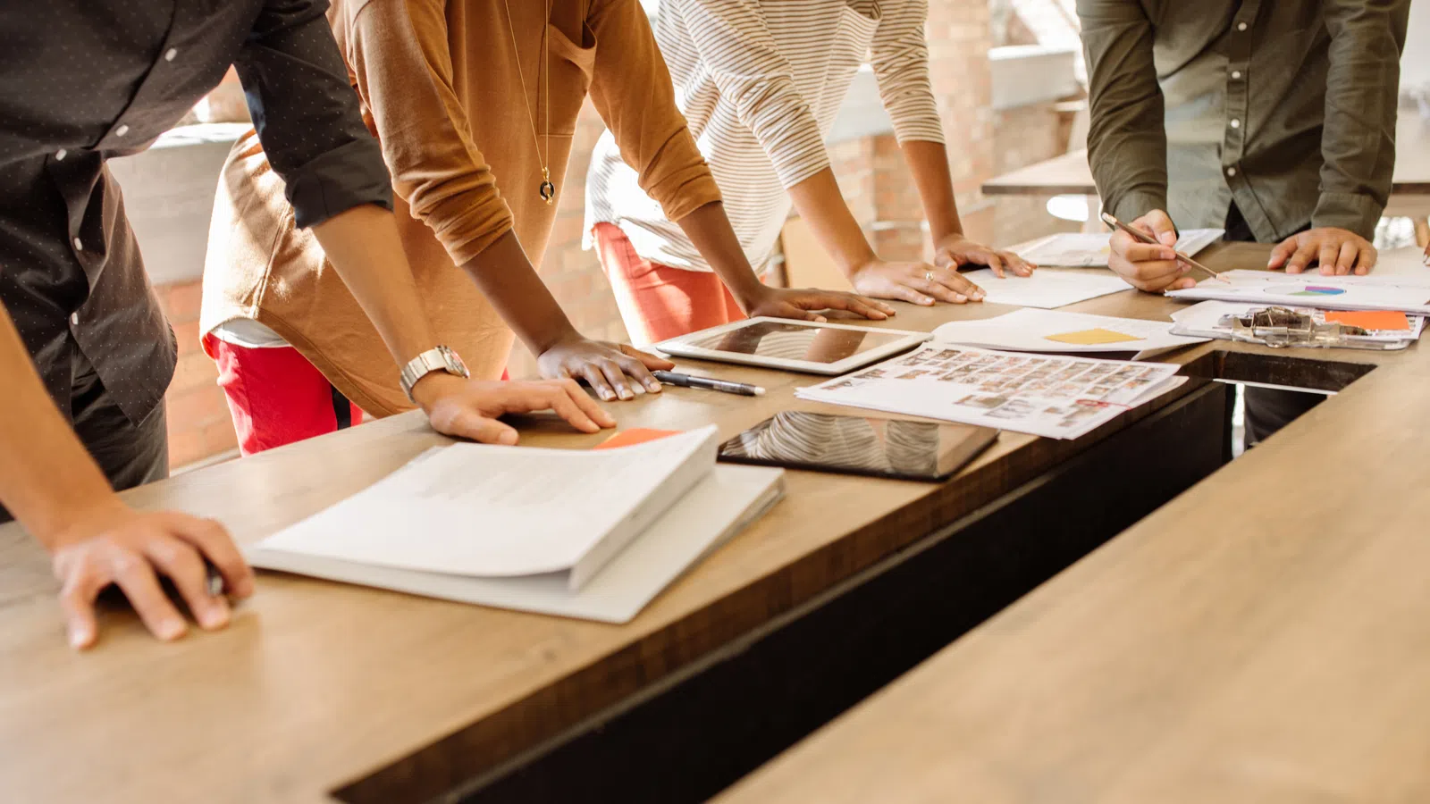 Group of diverse colleagues collaborating over documents and tablets around a wooden conference table in bright office