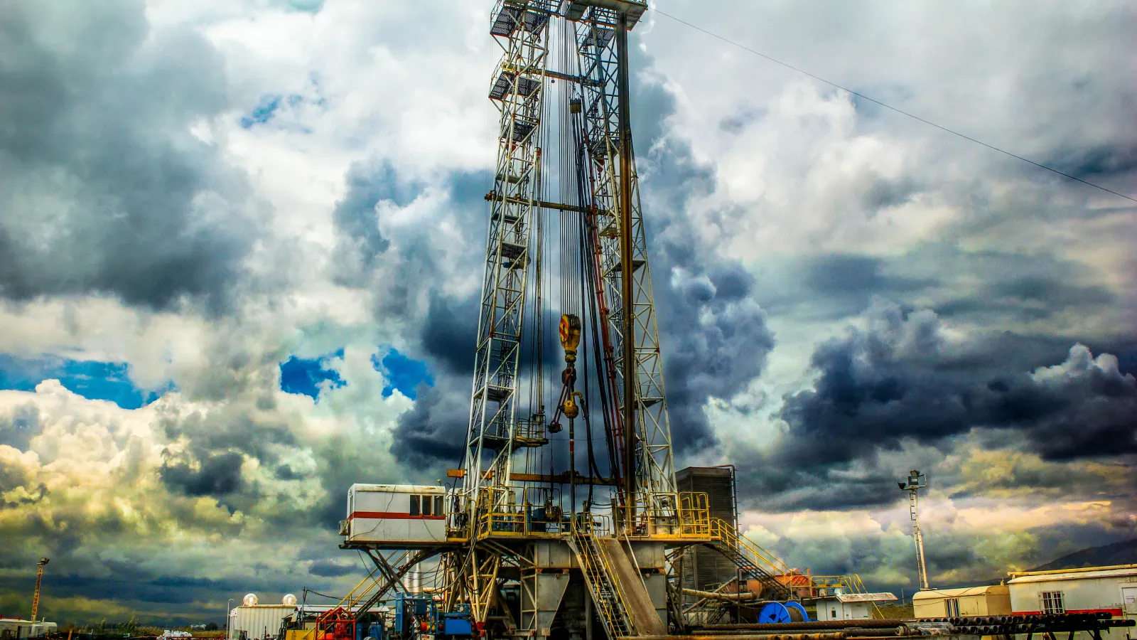 Oil drilling rig with machinery under a dramatic cloudy sky at an industrial site.