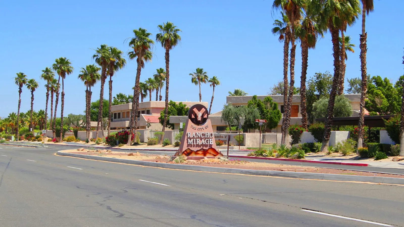 Entrance sign for Rancho Mirage with palm trees and residential buildings under a clear blue sky.
