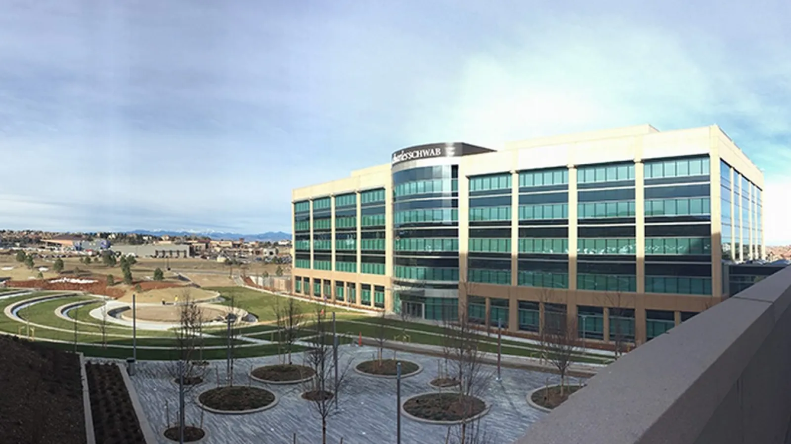 Modern office building with large windows, landscaped courtyard, and circular walkways under a clear sky.